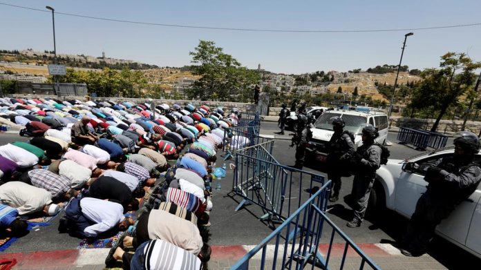 Palestinian Muslims pray outside of Jerusalem´s old city while Israeli police stand guard.