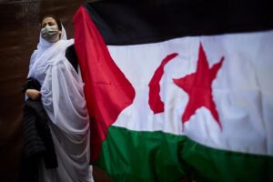 Caption: A Sahrawis holding the flag of Western Sahara in support of the Sahrawis’s right to self-determination .
