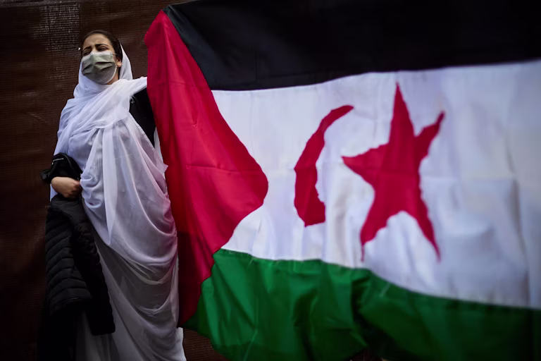 Caption: A Sahrawis holding the flag of Western Sahara in support of the Sahrawis’s right to self-determination .